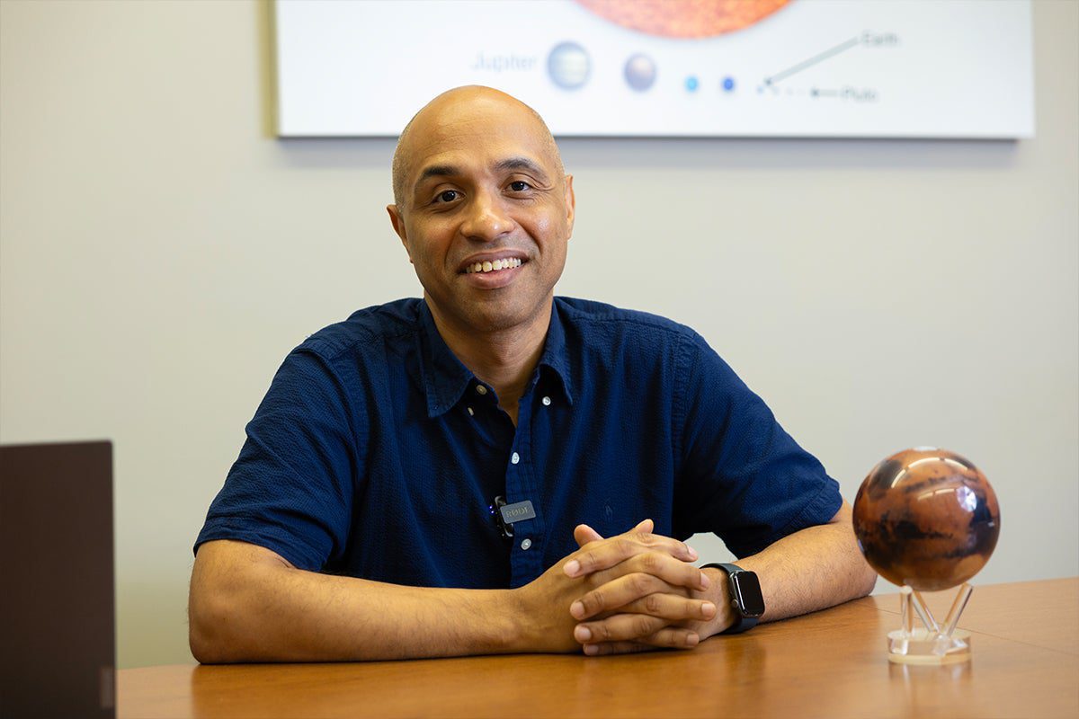 Photo of Prof. Ramses Ramirez sitting at a table with a Mars globe next to him.