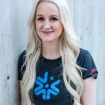 Person with long blonde hair wearing a Europa Clipper t-shirt, standing against a concrete wall.